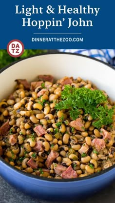 a blue bowl filled with beans and ham on top of a table next to parsley