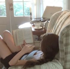 a woman laying on a couch reading a book