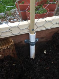 a pipe sticking out of the ground in front of a fence with potted plants behind it