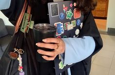 a woman holding a coffee cup in her hand and wearing a graduation gown with badges on it