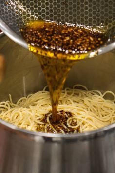 the sauce is being poured on top of noodles in a pot with a strainer