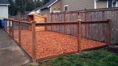 a wooden fence is in front of a house with red mulch on the ground