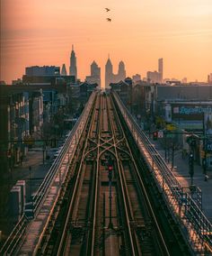 an aerial view of a train track and the city skyline in the background at sunset