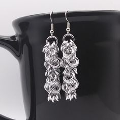 two pairs of silver earrings on top of a black mug