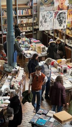 people looking at books in a bookstore with many shelves full of books and posters on the walls