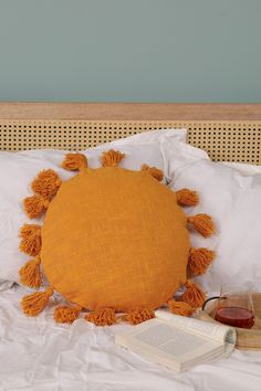 an orange pillow with tassels on it sitting on a bed next to a book