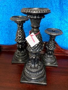 three metal candlesticks sitting on top of a wooden table next to a blue wall