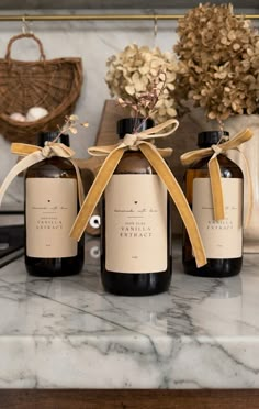 three bottles with labels tied to them sitting on a marble counter top next to flowers