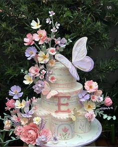 a three tiered cake with pink and purple flowers on the bottom, topped by a butterfly