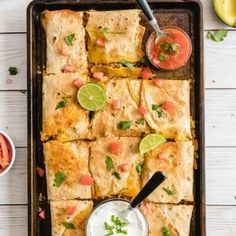 mexican food with tortillas, salsa and sour cream on a baking sheet next to some guacamole