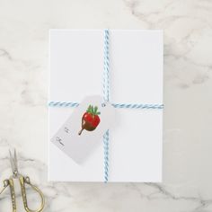 a gift wrapped in white paper with a strawberry on it next to scissors and a pair of scissors