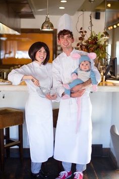 a man and woman in chef outfits holding a baby while standing next to each other