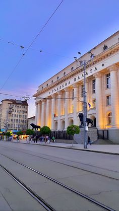 people are walking on the street in front of an old building with columns and pillars