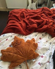 an orange stuffed animal laying on top of a bed next to a red comforter