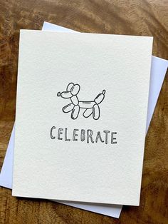 a card with the word celebrate written on it and a balloon dog in black ink