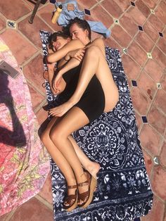 two women in swimsuits are laying on a towel and one is hugging the other