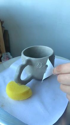 a person holding a sponge next to a cup on top of a table with a piece of paper in front of it