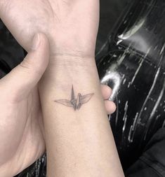 a small bird tattoo on the wrist is shown in black and grey colors, with one hand holding it up