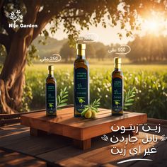 three bottles of olive oil on a wooden table in front of a field with trees