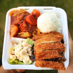 someone is holding up a takeout container with rice, meat and veggies