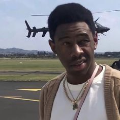 a man standing in front of an airplane with a helicopter flying above him on the tarmac