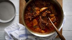 a pot filled with stew next to a wooden spoon on top of a cutting board