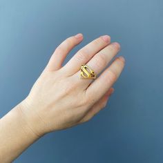 a person's hand with a gold ring on top of their finger, against a blue background