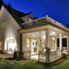 a white house lit up at night with lights on the porch and covered patio area