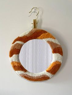 an orange and white wreath hanging on the wall next to a hook with a mirror in it