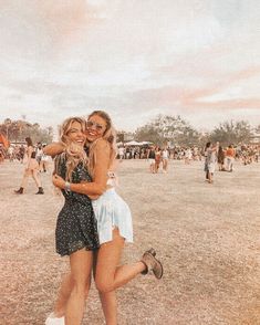 two women hugging each other in the middle of an open field with people walking around