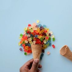 a hand holding an ice cream cone filled with gummy bears next to a scoop of ice cream