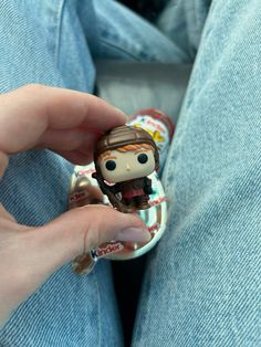 a person holding a tiny doll in their lap and wearing a button on the other hand