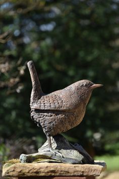 a bird statue sitting on top of a wooden table next to a forest filled with trees