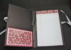 an open notebook with a notepad and pen on it next to a white ribbon