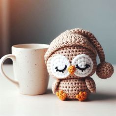 a crocheted owl sitting next to a coffee cup