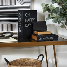 two books are sitting on a table next to a basket and potted plant in the corner