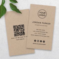 two business cards sitting next to each other on top of a white surface with a green plant