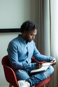 a man sitting in a chair writing on a piece of paper while holding a pen