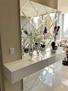 a mirrored table with vases and flowers on it in front of a large window