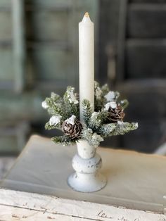 a candle that is sitting on top of a table with pine cones and evergreen branches