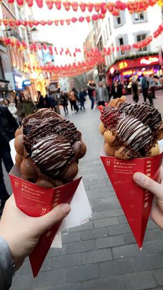 two people holding up pastries with chocolate frosting and drizzled on them