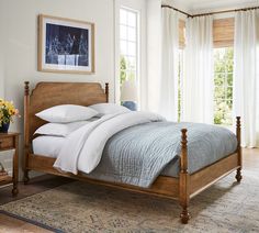 a bed in a bedroom with white linens and wooden headboard, along with two windows