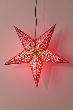 a red star shaped light hanging from a string on a pink wall next to a black cord