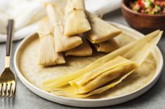 tamales on a plate with a fork and bowl of salsa in the back ground