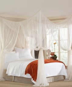 a white bed sitting in a bedroom next to a window with sheer curtains on it