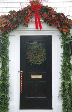 the front door is decorated with red flowers and greenery, along with wreaths