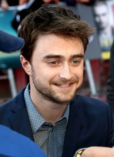 a man in a suit and tie smiling at the camera with other people behind him