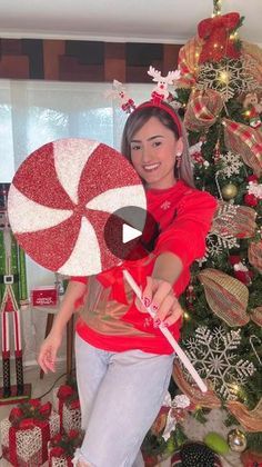 a woman holding a candy cane in front of a christmas tree