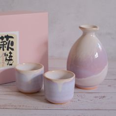 two white and pink vases sitting next to each other in front of a box