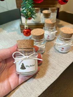 a hand holding a small glass jar filled with christmas tree scented candles next to other bottles